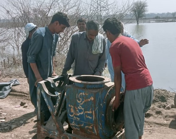 Three men look down into a metal container while more men work behind them.