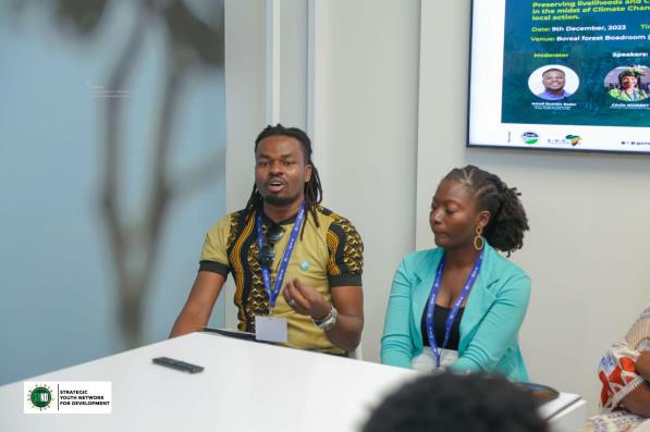 Two Black people sit together at a table. One of them is in the middle of speaking.