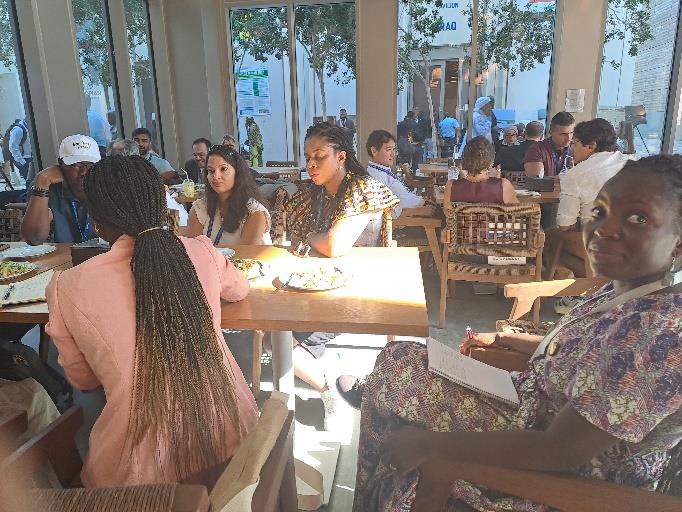 Greengrants staff and grantee partners sit together at a table in a cafeteria. The blog post's author, Nerissa Anku, is in the bottom right corner of the photo, looking at the camera.