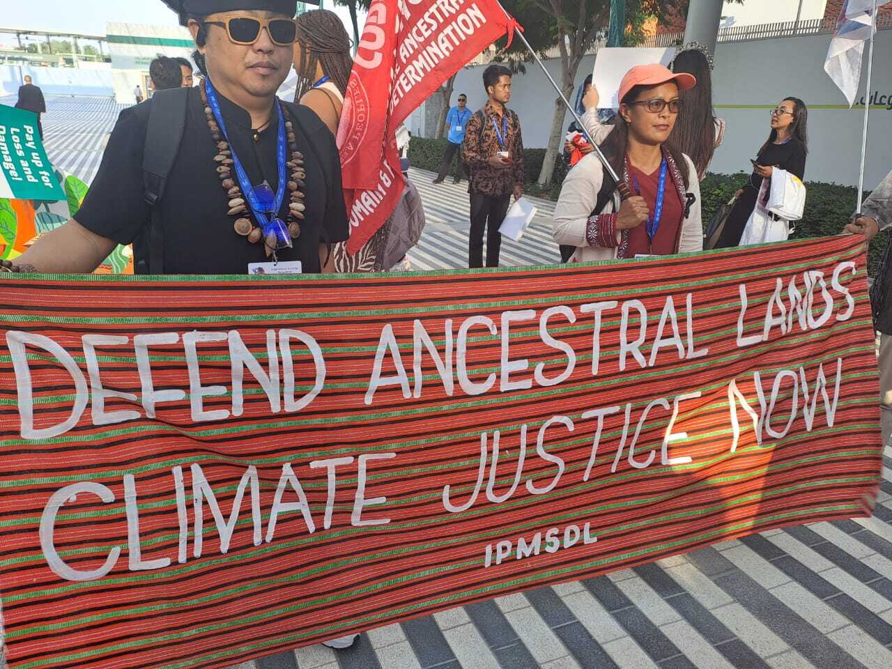 Two people stand with a large banner that reads "Defend ancestral lands, climate justice now."