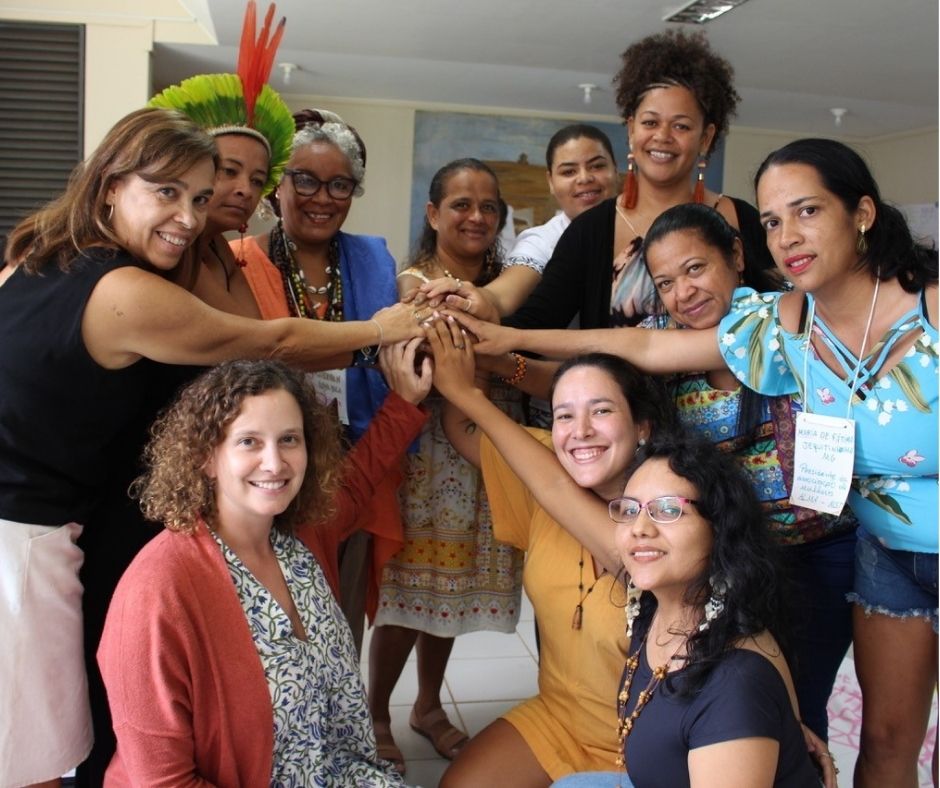 A photo of eleven women in Brazil posing together for the camera. They are leaning in so that their hands are touching, and many of them are smiling.