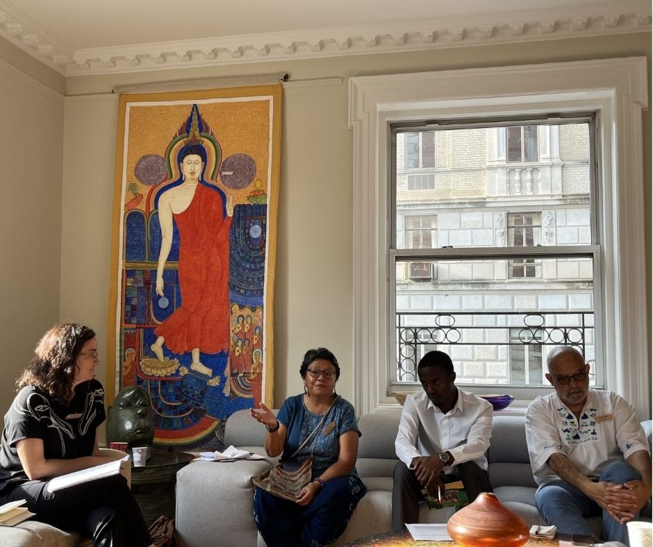 A photo of four panelists sitting together on couches. They are varied races and gender presentations. One of them, an Asian woman, is in the middle of speaking, gesturing with her hand.
