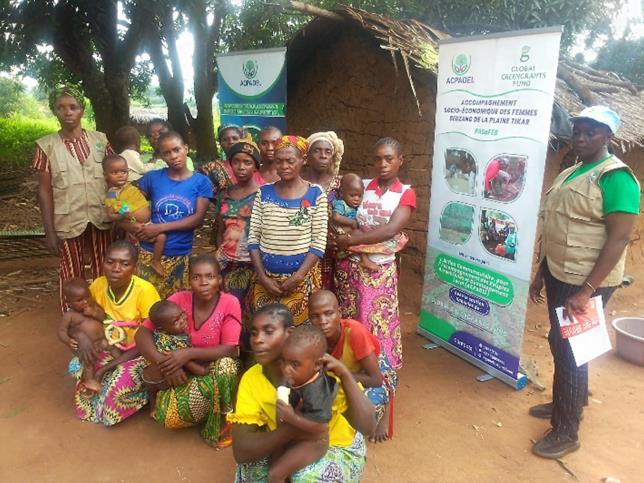 A group of about a dozen Black women wearing colorfully patterned clothing pose together for a photo, many of them holding babies. 
